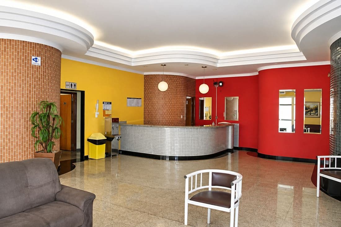 Recepção do velório da Pax Vida, com balcão de atendimento curvo, poltronas e paredes em vermelho e amarelo